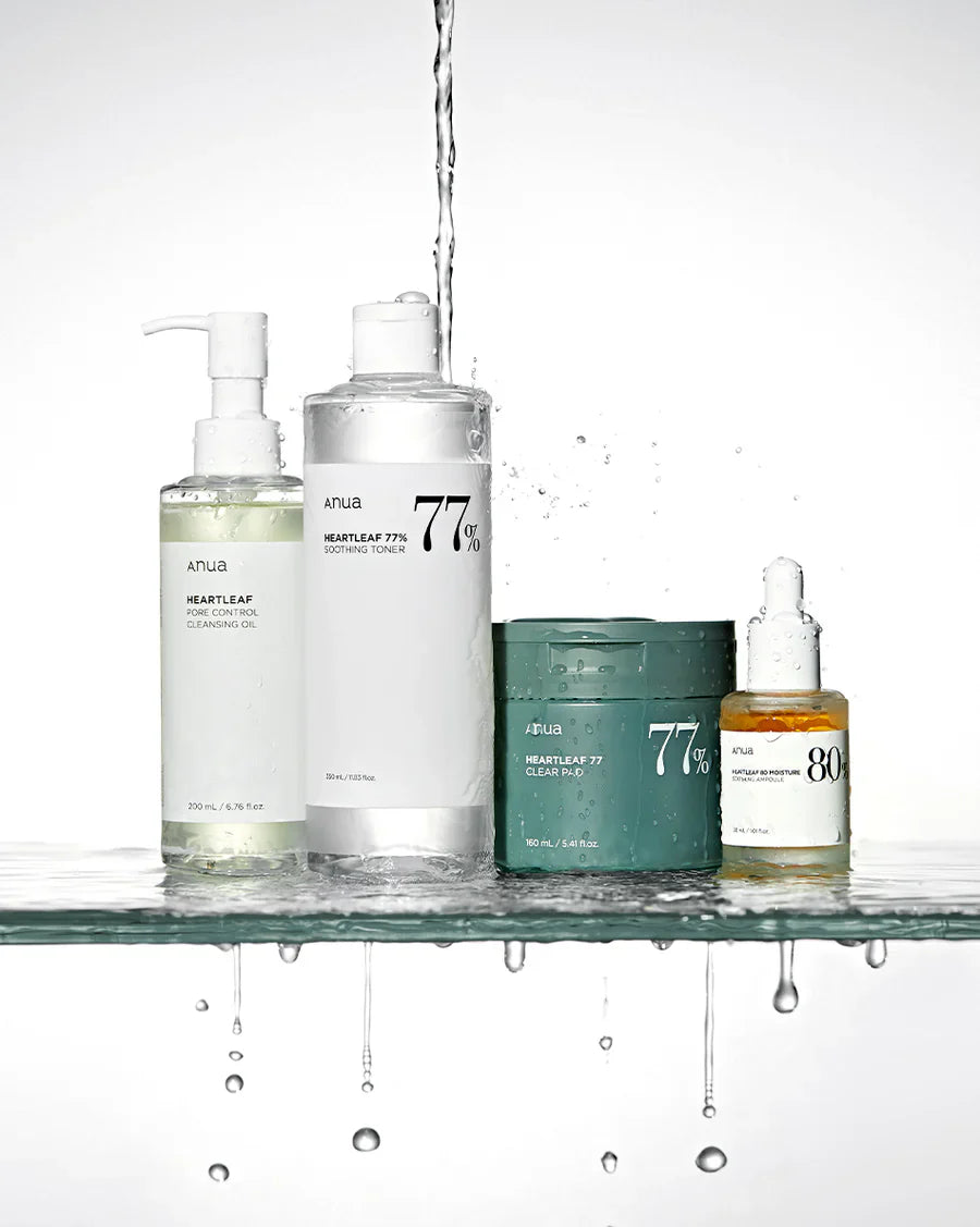 Selection of products from Anua, including an oil cleanser, toner, toner pads and ampoule, from Anua’s Heartleaf collection. There is water being drenched onto them, possibly signifying their hydrating and pure properties.